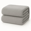 Een netjes opgevouwen Teddy fleece hoeslaken - 90x200 cm, lichtgrijs en extra warm, op een effen witte ondergrond.